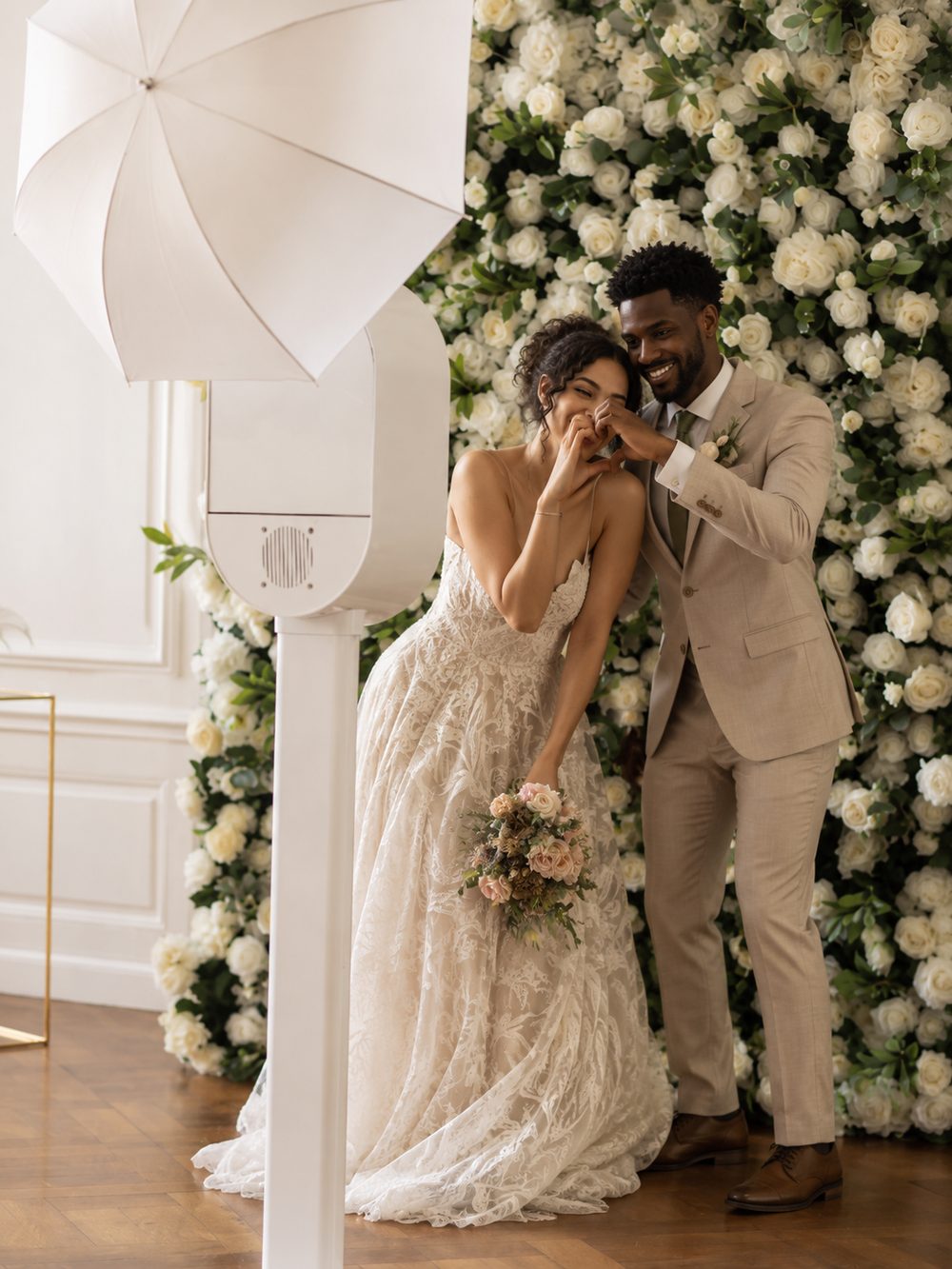 Bride and groom sharing a moment beside the Pearl & Zee luxury photo booth, in front of a white rose flower wall